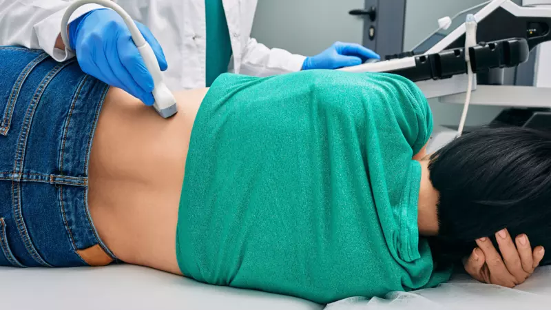 A lady on her side while a doctor scans her kidney using an ultrasound probe. 